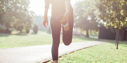 a person holding their leg stretching at a park with grass and a pathway
