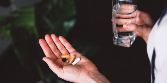 a person holding out their hand with supplements scattered with a glass of water