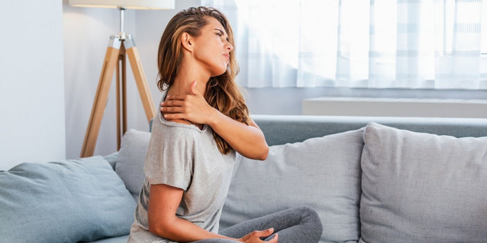 a woman sitting crosslegged on a a couch holding her stiff neck